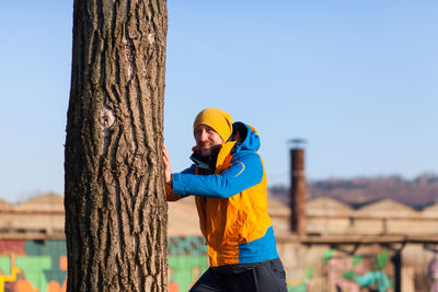 Portrait of mid adult man standing by tree against clear sky