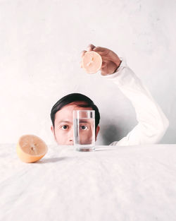 Portrait of man holding lemon over glass of water on table
