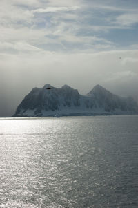 Scenic view of sea by mountain against sky