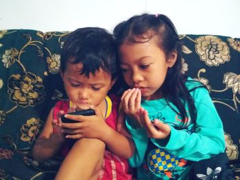 Siblings looking at camera while using phone at home