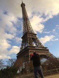 Rear view of man carrying baby while looking at eiffel tower against sky