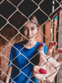 Portrait of young woman standing by chainlink fence