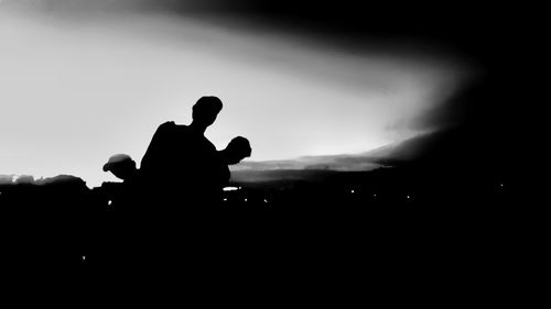 Rear view of silhouette men sitting against sky during sunset