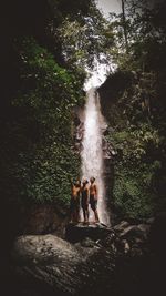 People standing by waterfall in forest