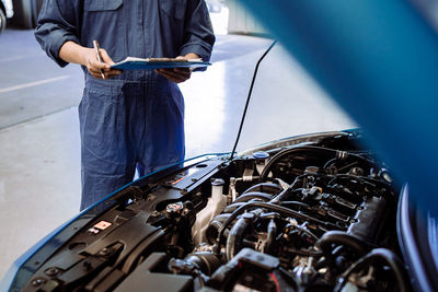 Midsection of mechanic examining car