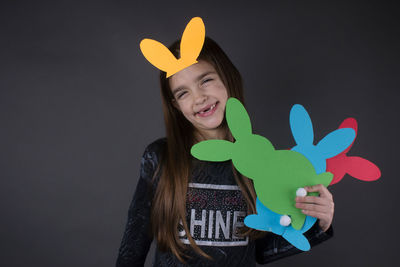 Portrait of smiling girl with eater bunny and pom pom in basket against gray background