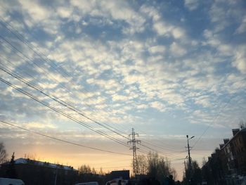 Low angle view of silhouette electricity pylon and buildings against sky