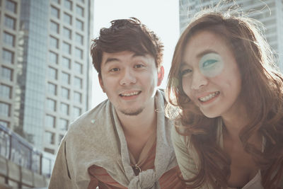 Portrait of smiling young couple against buildings in city