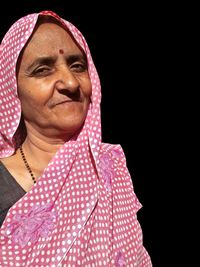 Close-up portrait of mature woman wearing pink sari against black background