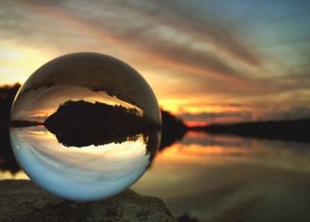 Close-up of crystal ball against sea during sunset