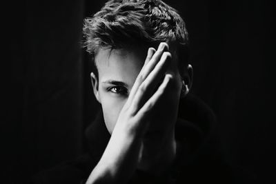 Portrait of man covering face while standing against black background