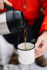 Low section of person pouring tea in cup on snow covered field