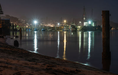 Illuminated city by river against sky at night