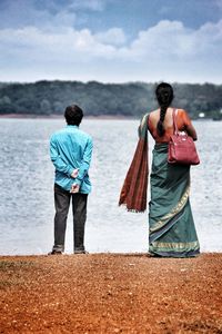 Rear view of young couple standing on beach against sky