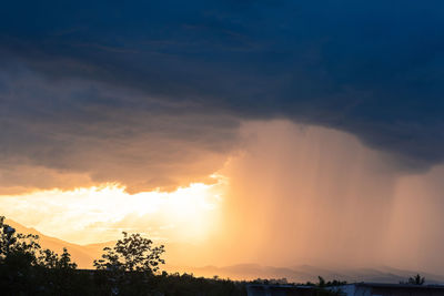 Sunlight streaming through silhouette trees against sky during sunset