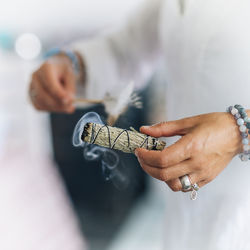 Midsection of sage holding feather with smudge stick while standing indoors