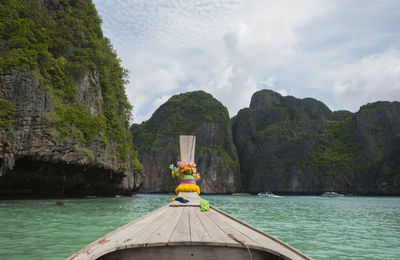 Longtail boat in sea against rocky mountains