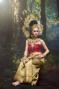 Portrait of beautiful young woman in apsara costume sitting in forest