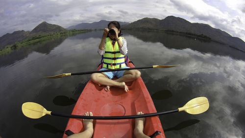 Woman photographing while sitting on kayak in lake