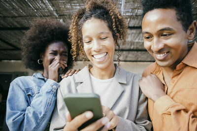 Happy woman sharing mobile phone with friends at backyard