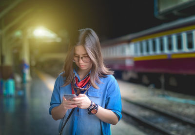 Woman using mobile phone while standing at railroad station platform