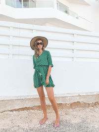 Full length portrait of young woman standing against wall