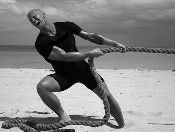 Full length of man pulling rope while standing on sand at beach