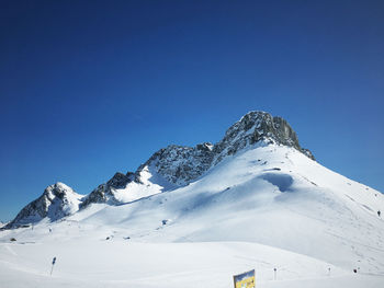 Low angle view of snowcapped mountains against clear blue sky