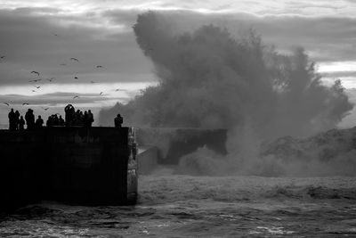 Tourists on beach against cloudy sky