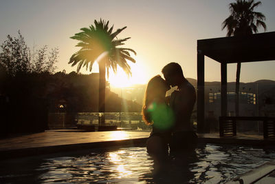 Silhouette people by swimming pool against sky during sunset