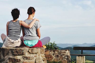 Lesbian couple sitting on wall against sky