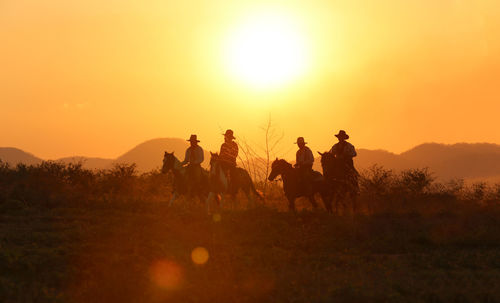 People riding horses on field against sky during sunset