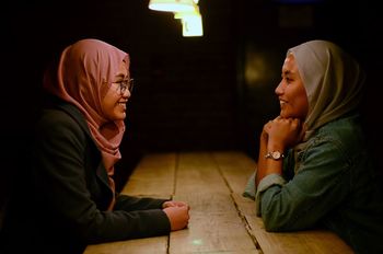 Side view of smiling women in headscarf talking on table