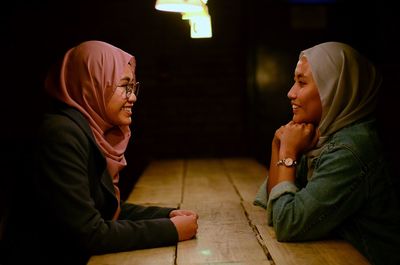 Side view of smiling women in headscarf talking on table