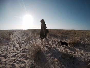 Woman walking with chihuahua on sand at beach against sky