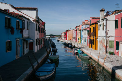 Boats moored on canal amidst houses in city