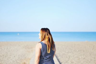 Rear view of woman at beach against clear sky