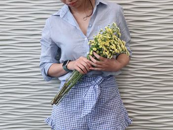 Midsection of woman holding flower bouquet against wall