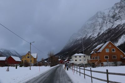 Road amidst snow covered houses and mountains against sky