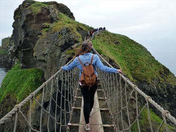 Rear view of woman on footbridge against sky