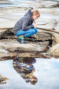 Side view of young woman crouching on rocky shore