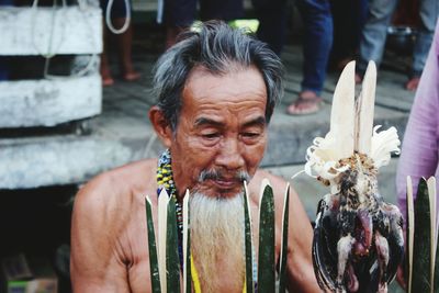 Close-up of shirtless senior man with equipment sitting outdoors