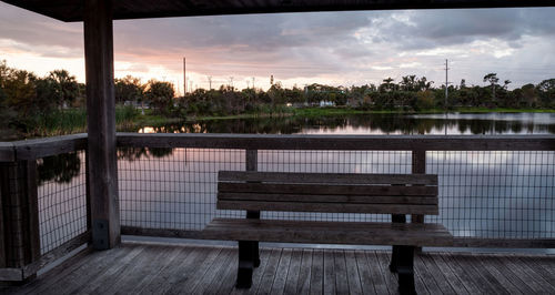 Bench by railing against sky during sunset