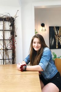Portrait of smiling young woman sitting on table at home