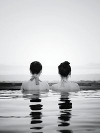 Rear view of girls enjoying in swimming pool against clear sky