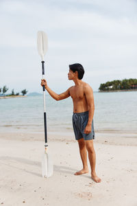 Rear view of shirtless man with surfboard at beach