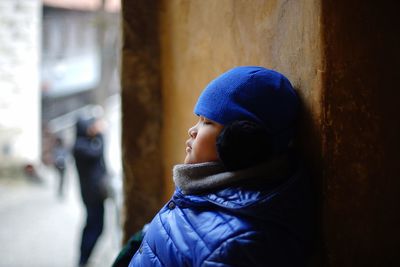 Profile view of boy wearing warm clothing while leaning on wall