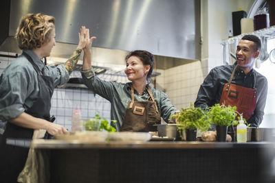 Happy male chef looking at female colleagues giving high-five in restaurant kitchen