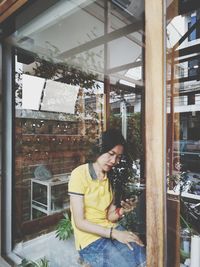 Woman using mobile phone in cafe seen through window