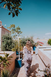 Rear view of woman standing by swimming pool against sky